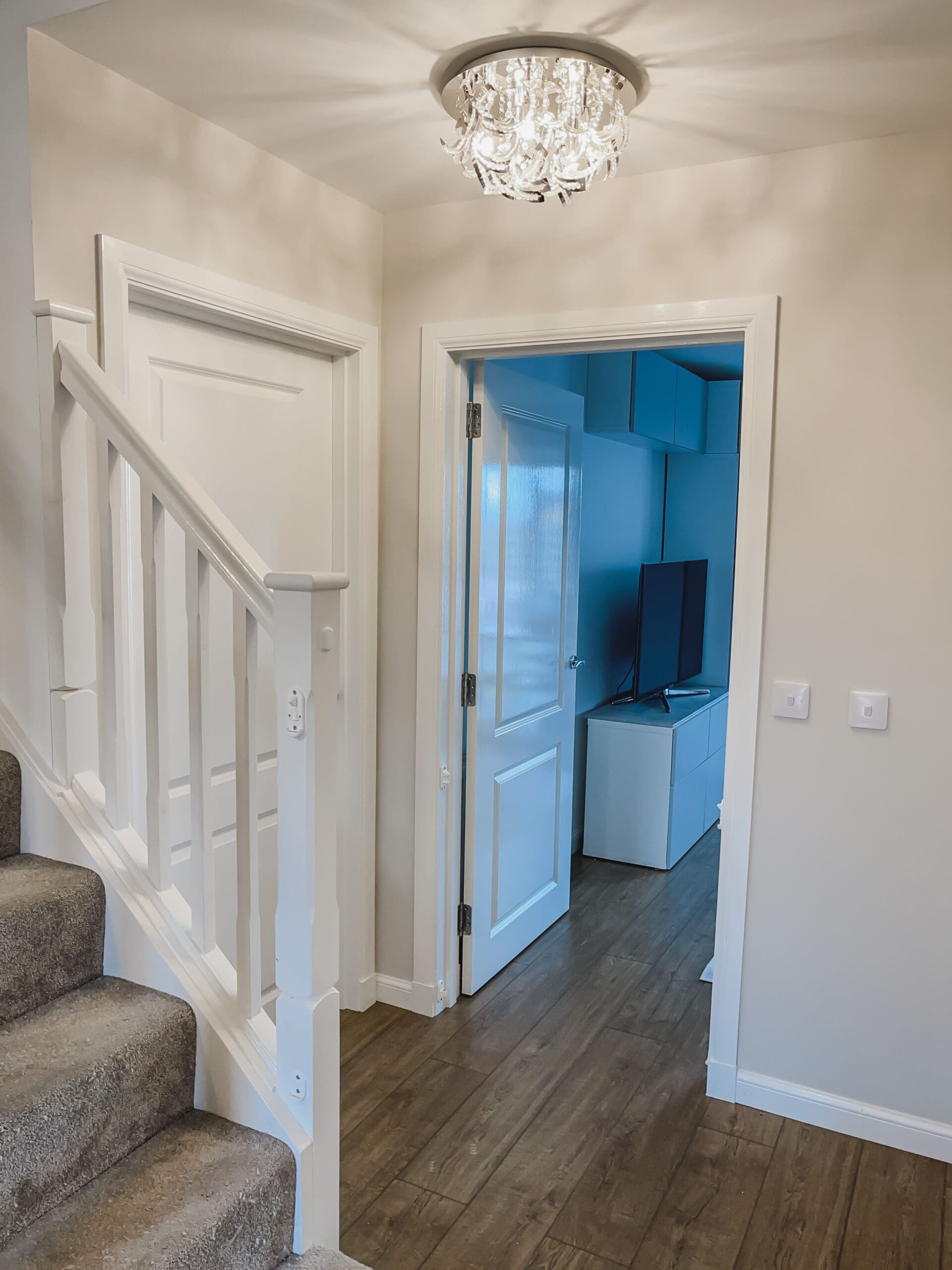 Hallway view past the staircase showing crystal ceiling light, Valspar Goose Feathers walls and wooden flooring