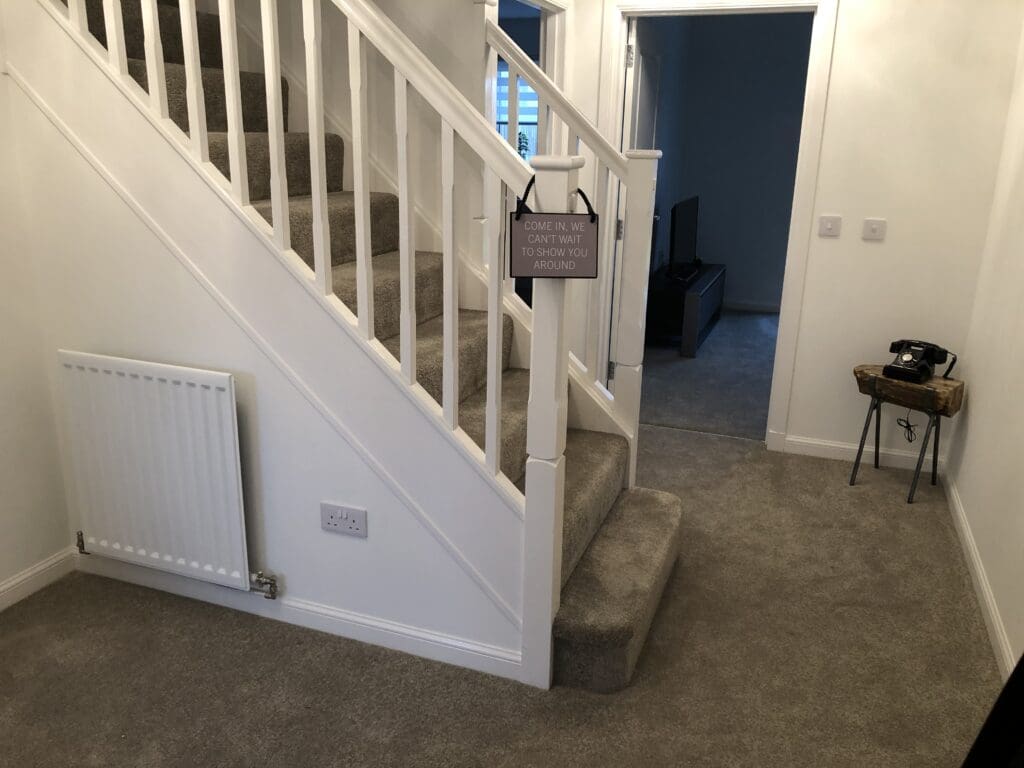 Hallway before the makeover with grey carpet, white walls and staircase with Come In sign