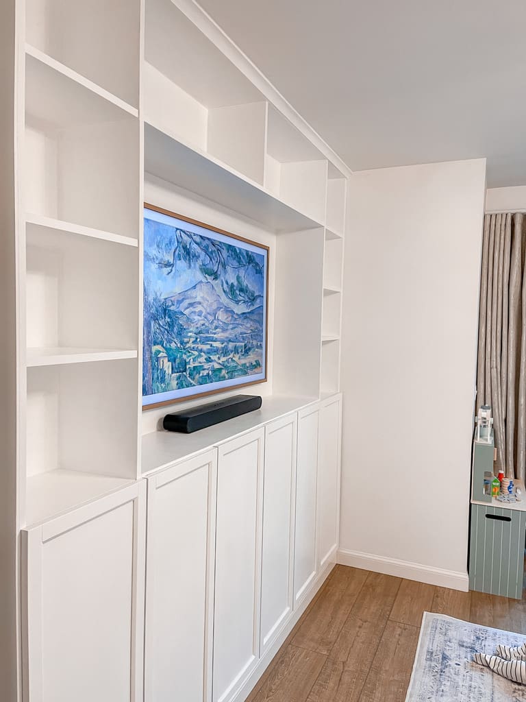 Custom built-in shelving made from white IKEA Billy bookcases with cabinets and open shelves around a wall-mounted Frame TV.