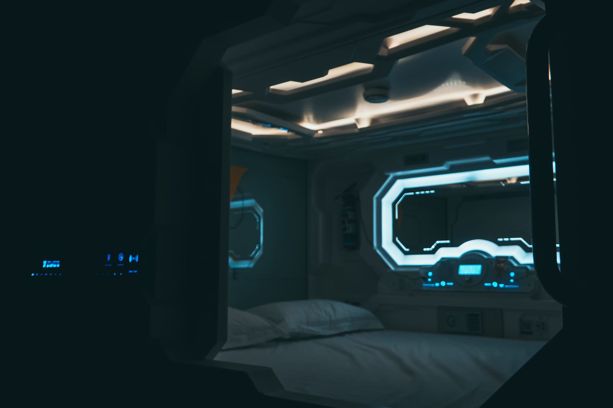 Inside view of a sci-fi style capsule pod at the Yellow Capsule hotel Cancun, with glowing blue lights and a porthole window