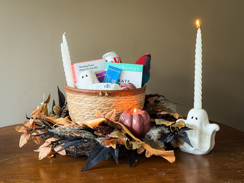 A finished boo basket styled on a wooden table with an autumn wreath, lit taper candle and ceramic ghost candle holder