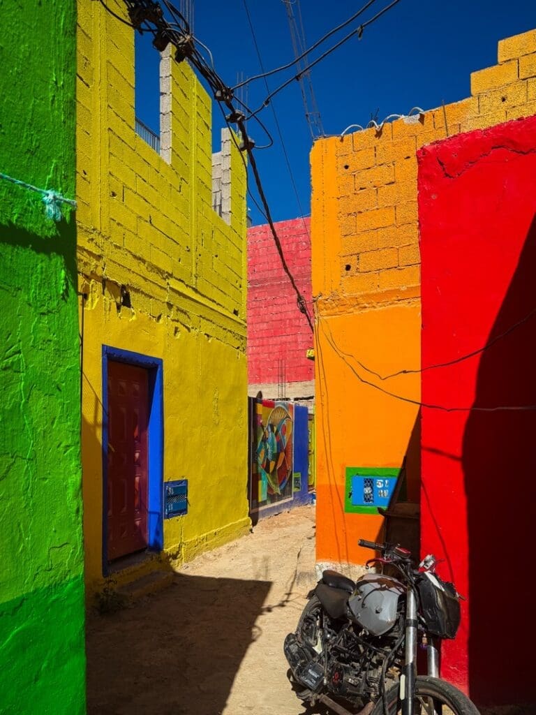 Narrow lane between green, yellow and red houses in Aghroud, with a motorbike parked outside