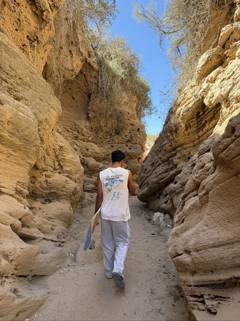 Guide carrying a sandboard along a narrow path between rocky canyon walls near Agadir