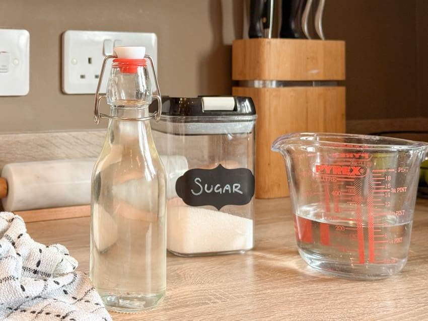 Homemade simple syrup in a swing-top glass bottle beside a sugar container and measuring jug
